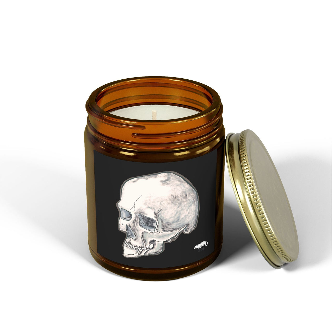 An amber glass jar filled wit ha candle. The glass has a black decal on it with a white skull. The lid is off the jar and is leaning on the jar 