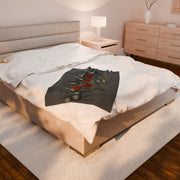 A neatly made bed features a white mattress and light-colored headboard, exuding gothic elegance. The Gothic Floral Velveteen Plush Blanket in Dark Grey by Printify drapes over the bed. A nightstand with a lamp and a wooden dresser completes the cozy ambiance.