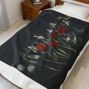 The Gothic Floral Velveteen Plush Blanket - Black by Printify features red and white tulips with green stems on a black backdrop, subtly incorporating a skull design. It complements wooden furniture and light-colored flooring, offering a touch of gothic elegance.