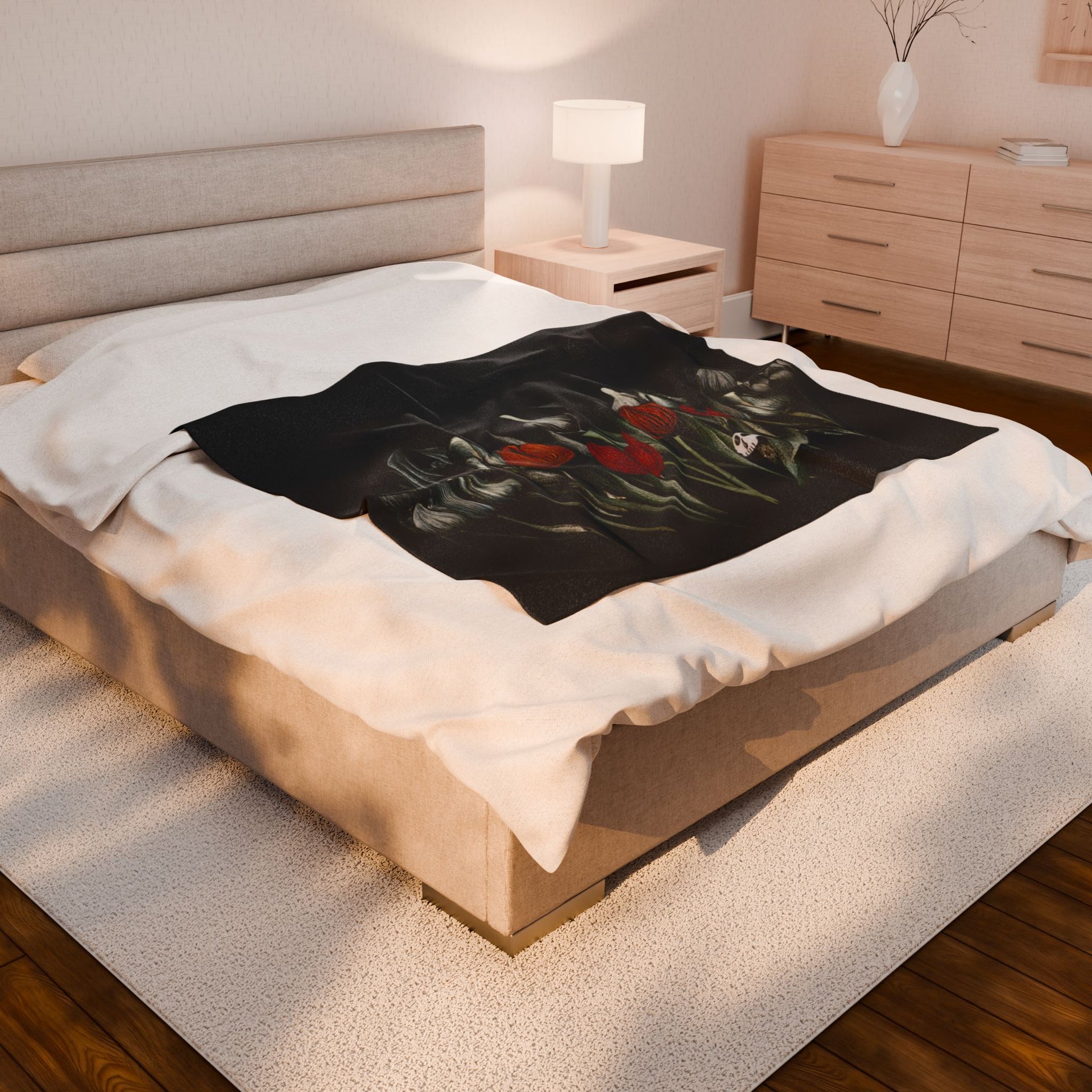 The bedroom showcases a large bed with the Gothic Floral Velveteen Plush Blanket by Printify and velveteen pillows. A wooden nightstand with a lamp stands beside it, while a classic dresser and soft rug on the wooden floor add to the rooms cozy gothic elegance.