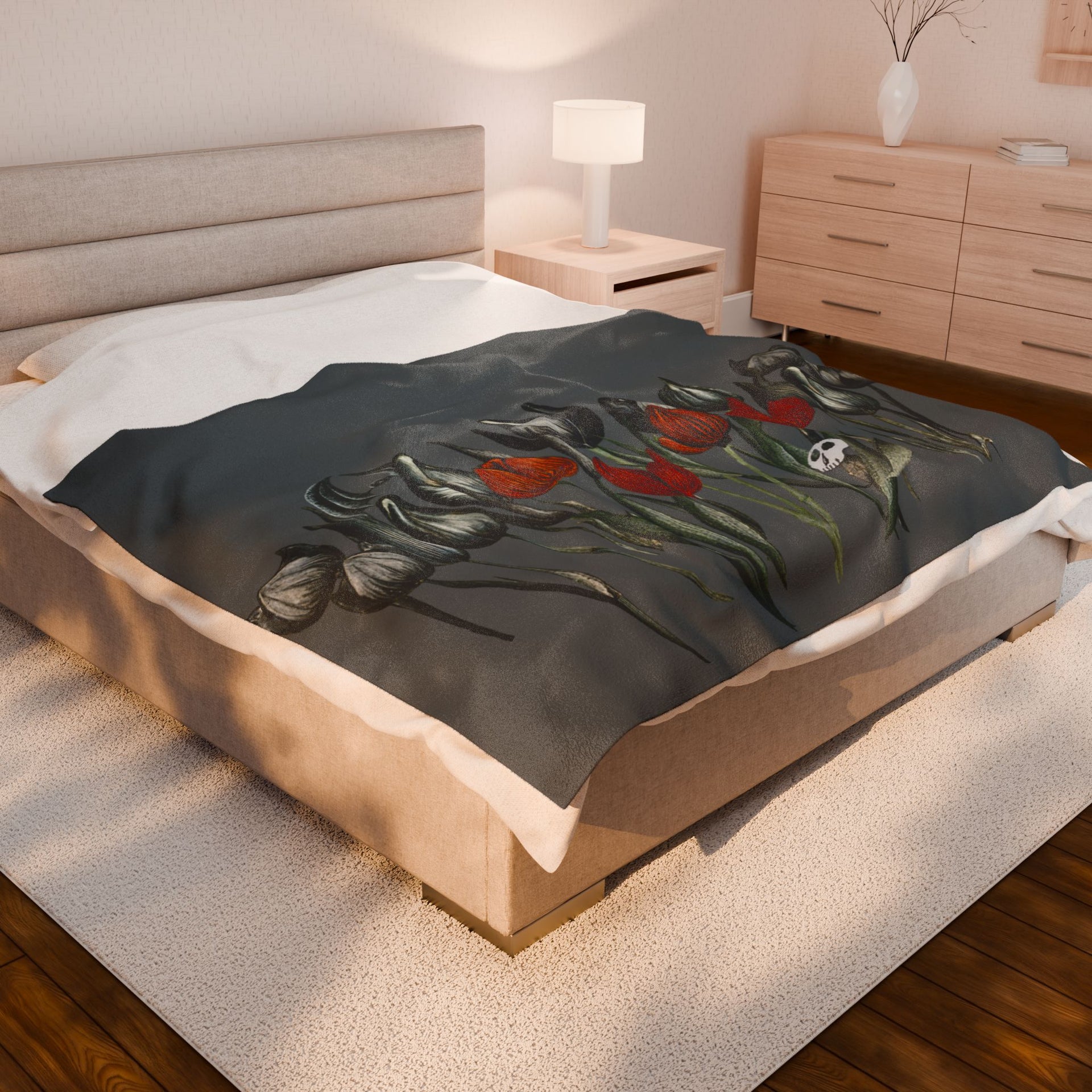 A bedroom featuring a Printify Gothic Floral Velveteen Plush Blanket in dark grey, with red tulips, green leaves, and a subtle skull on a velveteen platform bed. The room includes light wooden furniture, a soft rug, a lamp, and a minimal decorative vase.