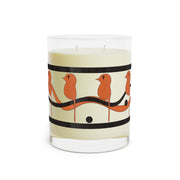 The Printify Dream Bird Candle in blood orange features orange bird designs on black branches encircling a clear glass container. This scented candle is crafted with soy wax and has two wicks, offering cream-colored wax for a delightful aromatherapy experience and 65 hours of burn time.