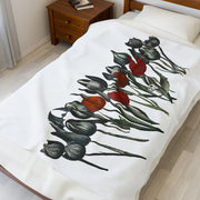 The Printify Gothic Floral Velveteen Plush Blanket in white features an artistic design of black and red flowers with green stems, capturing gothic elegance. It covers a bed within a room featuring a wooden nightstand with books and a window dressed with white curtains.