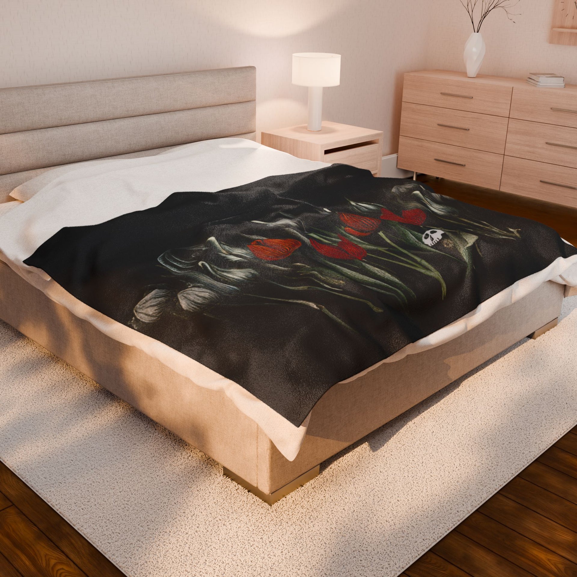 A modern bedroom exudes gothic elegance with the Printify Gothic Floral Velveteen Plush Blanket - Black, featuring a red tulip and skull design. The light wood theme includes a bedside table, lamp, and dresser adorned with a branch-filled vase. A cozy rug accents the wooden floors.