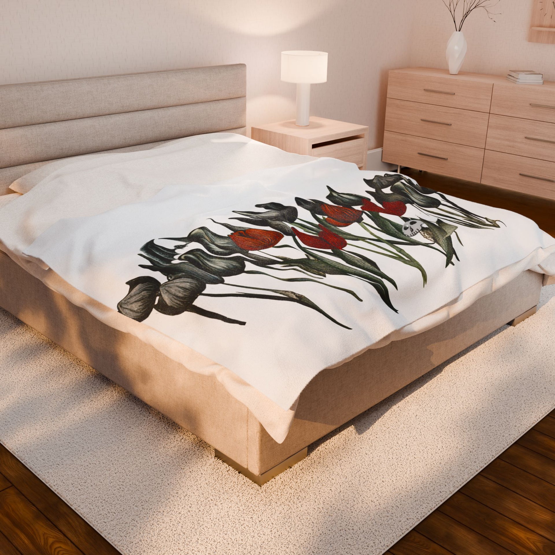 A cozy bedroom features a beige bed with the Gothic Floral Velveteen Plush Blanket in red and black from Printify, complemented by a wooden nightstand and lamp. A creamy rug softens the wooden floor, enhancing the blankets gothic elegance.